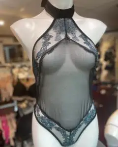 A black sheer halter-style bodysuit displayed on a mannequin, featuring intricate blue floral lace accents along the neckline and hips. The bodysuit has a high neckline with a velvet choker collar, creating an elegant and dramatic look.