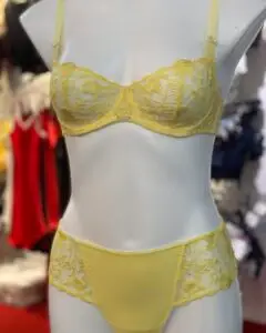 A delicate yellow lingerie set featuring a sheer lace bra with floral embroidery and matching lace-accented panties, displayed on a mannequin in a boutique setting.